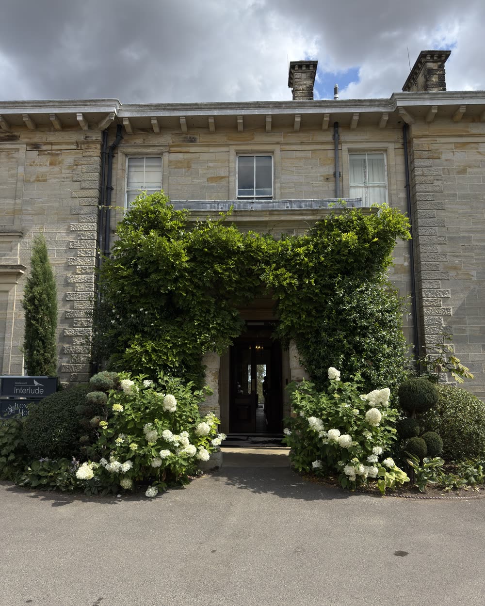 Ivy covered entrance of a stone country house banked with white hydrangeas