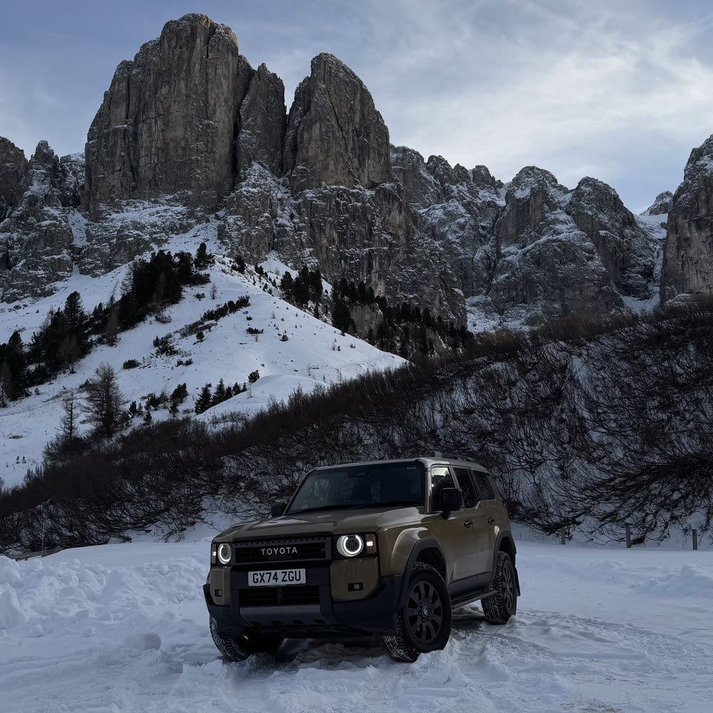 Toyota Land Cruiser parked in snow below mountain peaks